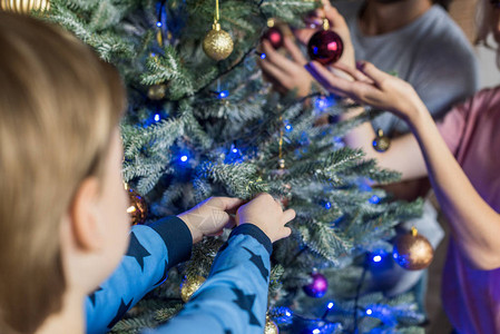 父母与小儿子一起把圣诞树装饰在一起背景图片