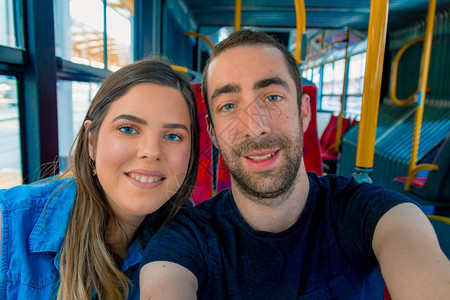 快乐的一对夫妇在一辆城市公共汽车上拿着智能手图片