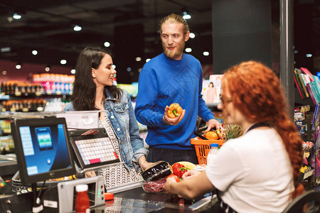 在现代超市一起购买产品快乐的一对年轻夫妇在收银台附近站立图片