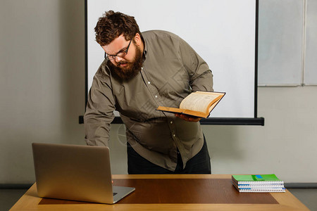 带书和笔记本的有照片的成人教师在桌子上用笔记本电脑工背景图片