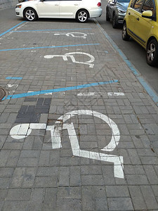 在汽车自然光轮椅符号之间的几个地方的瓷砖街道上为残疾人提供背景图片