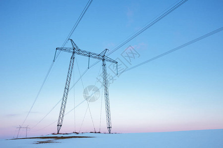 柔和的日落时空旷的冬田中的电力线图片
