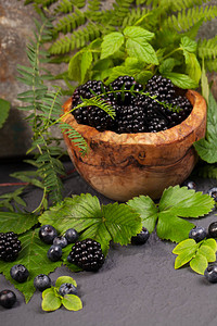 新鲜的黑莓和蓝莓木碗里有绿叶图片