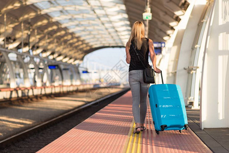 在火车站平台上行走并等待火车的有蓝色行李手提图片