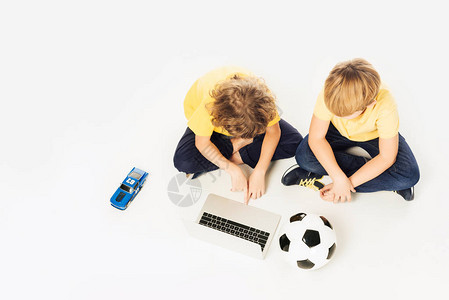 两个小男孩在与白色孤立的玩具一起坐着时使图片