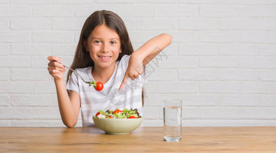坐在桌子上吃健康沙拉的年幼西班牙小孩以手和指图片