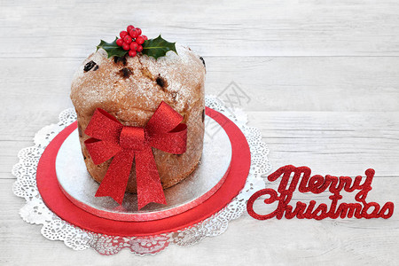 蛋糕与红色闪光蝴蝶结和圣诞快乐标志与质朴的木上的冬青树图片