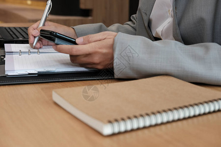 男人在笔记本上写提醒日程表商人在工作场所联合办公用智能图片