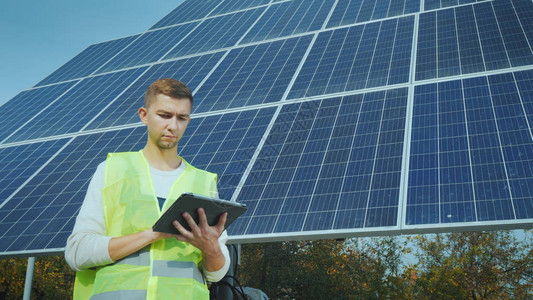 一名年轻的工装程师在一个大型太阳能电池板附近图片