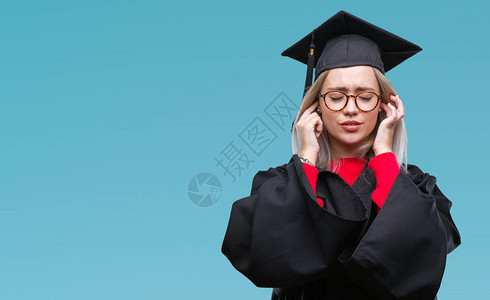 身着研究生制服的金发年轻女子在孤立的背景下用手指遮住耳朵图片