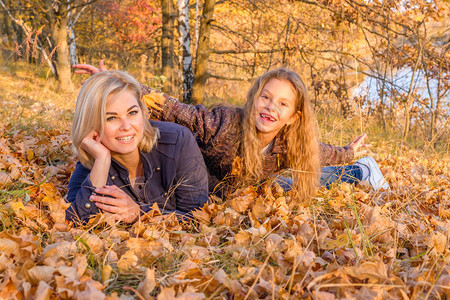 年轻美丽的母亲和她可爱的小女儿躺在秋天的落叶上图片