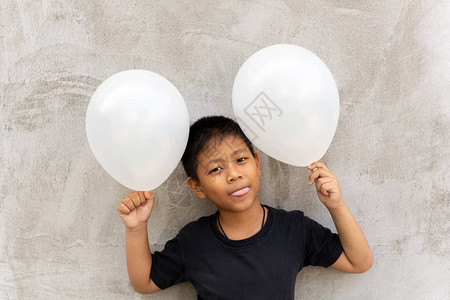 小亚洲小男孩拿着白气球在灰背景图片