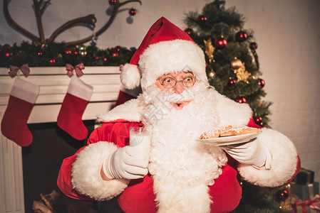圣诞老人拿着饼干和牛奶杯的盘子图片