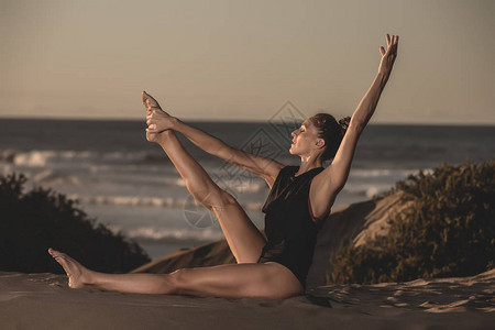 坐在阳光下的沙上穿着美丽姿势做瑜伽的优美体贴美丽的女图片