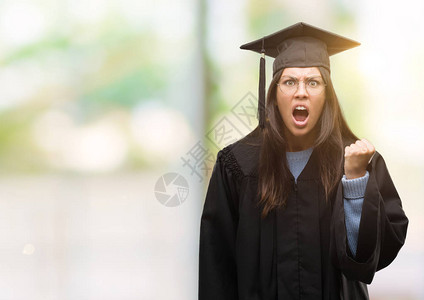 年轻的西班牙裔妇女戴着毕业帽和制服愤怒和疯狂地举起拳头沮丧和愤怒图片