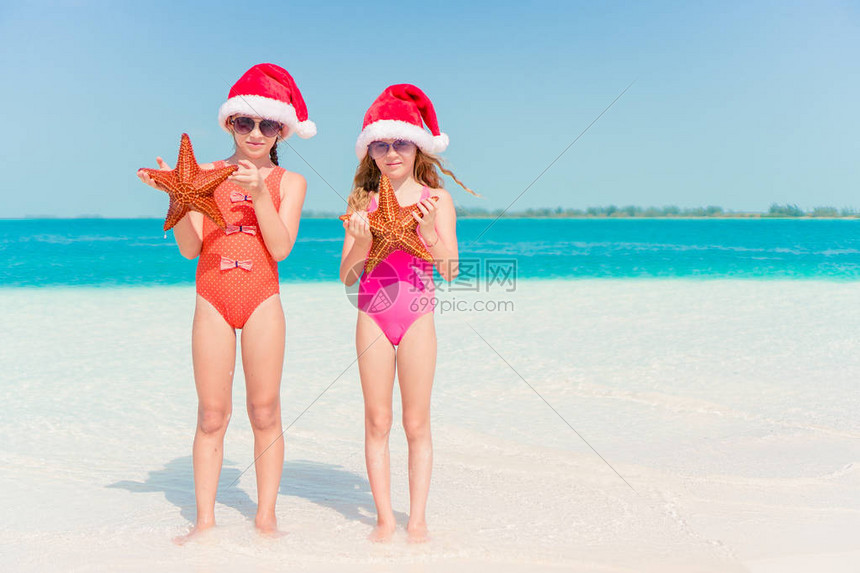 穿着圣诞帽子的小女孩在白沙滩上与海星一起度过图片