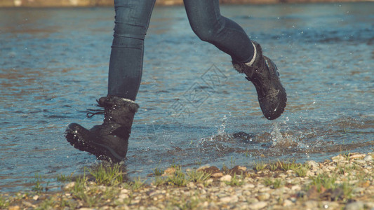 穿着毛茸的靴子沿着平静的溪流奔跑的不知名女人的电影镜头图片