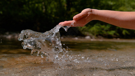 未知的年轻女子的手在清澈的河水中溅起水花图片