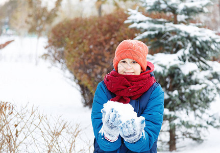 穿着红色帽子蓝色夹克的可爱小男孩拿着和玩雪图片