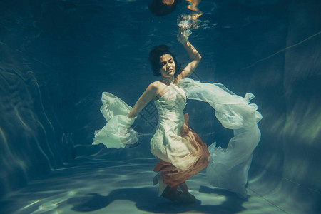优雅的苗头女孩在水下游泳就像一个自由潜水者穿着白色晚礼服图片