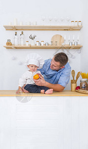 父亲给戴厨师帽的小儿子美味的橙子父亲节假期为人父母的童图片