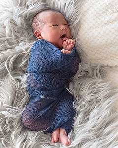 可爱的亚洲新生婴儿男孩被披着长毛毯裹在地毯上的紫编织的摩海发包中卷起来背景图片