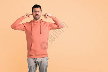 穿着粉红色运动衫的男人用手捂住两只耳朵赭石背景图片