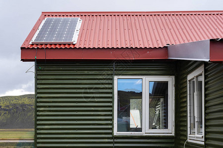 顶上安装有红色铆钉屋顶和太阳能电池板的绿色小型舒适屋的照片图片