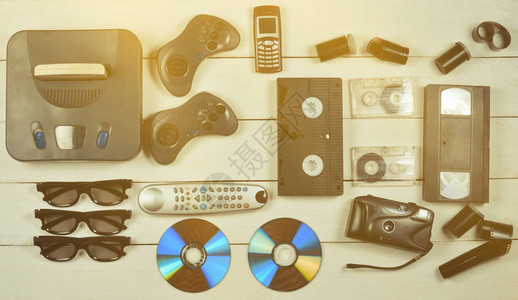 娱乐90年代游戏机游戏手柄磁盘录音带录像带电话白色木桌上的胶卷相机图片