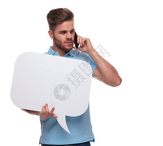 身穿蓝色马球衫手持讲话泡站在白色背景上一边打电话一边低头看向一边的背景图片