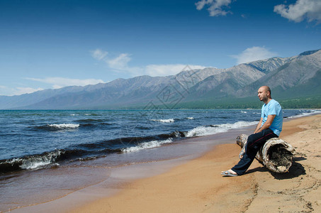 男人们坐在俄罗斯巴古津湾Baikal湖附近海滩上一个非常古老的木质腐背景图片