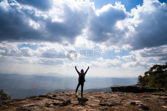 一个人举起手站在岩石山上看着风景优美的自然景色和图片