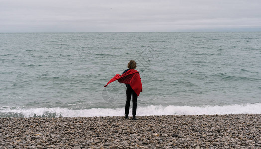 穿着红色斗篷站在海边做梦和享受美丽的风景的女旅行者背影图片