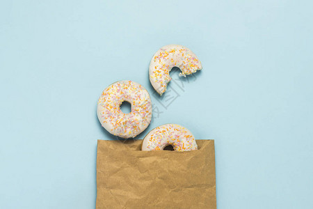 蓝色背景上的纸袋和新鲜美味的甜圈快餐面包店早餐糖果的概念极简主义图片