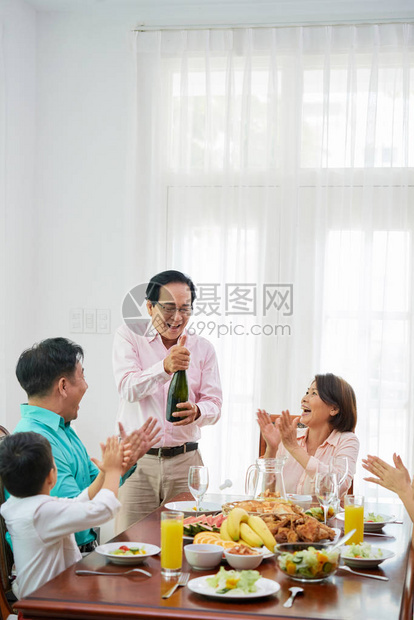 兴奋的老人在家庭晚餐桌上开香槟酒瓶图片
