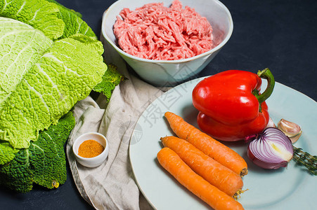 萨沃伊卷心菜卷的配料胡萝卜甜椒洋葱大蒜百里香料米饭碎牛肉深色背景图片