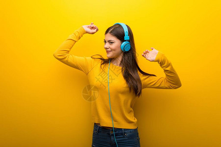 用耳机和舞蹈收听音乐的年轻女孩在充满活力的黄色背图片