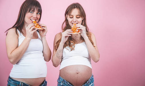 两个漂亮的孕妇在粉红色背景下吃披萨图片