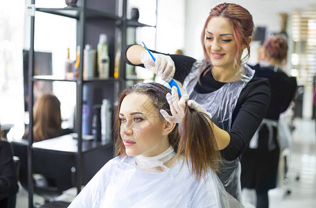 专业女美发师在设计美发沙龙为女顾客涂色图片