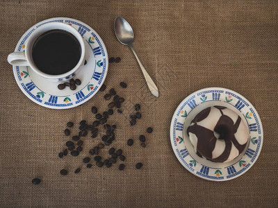 一杯瓷茶一勺古董汤匙巧克力甜圈和咖啡豆的早餐图片