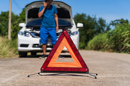一个人在路上有一辆麻烦的汽车和红色三角警告标志时使图片