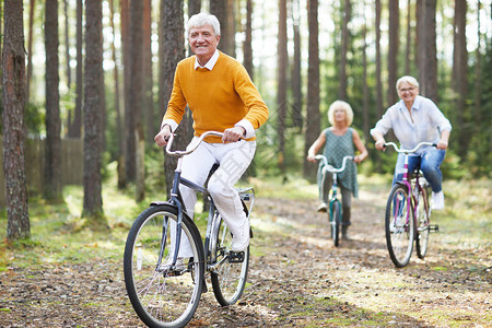 穿着休闲服的快乐兴奋的老朋友们在森林里一起骑自行车享受积极的生活图片