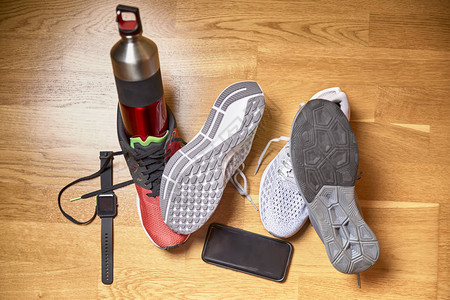 在健身房木制地板上水瓶和技术配件旁边运动鞋的图片