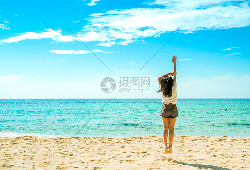 穿着白衬衫和短裤的快乐年轻女子在沙滩上跳跃在蓝天白云的热带天堂海滩放松和享受假期暑假的女孩夏日风情图片