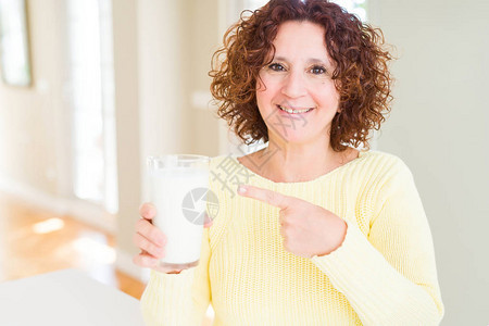 喝一杯新鲜牛奶的年长妇女以手和指图片