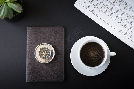 办公桌顶部视图或平板布满黑色背景白色键盘咖啡杯金属罗盘和图片