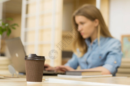 有选择地关注桌子上的咖啡纸杯年轻女在背景复制空间办公室合作工区教育技术在线电子概念图片