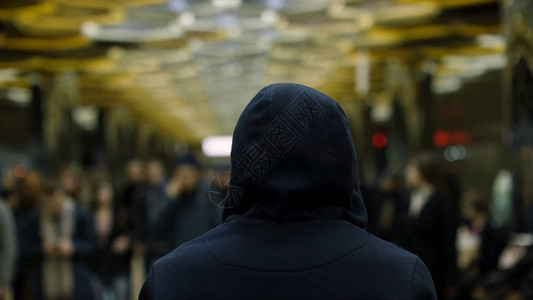 一名身穿深蓝色连帽衫的男子站在车站人群面前的后视图片