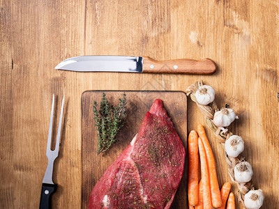 大蒜胡萝卜和厨师刀旁边一大块红肉的顶端在框架中央图片