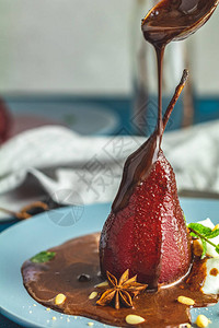 巧克力酱从勺子里倒在酒里的红梨上红梨放在蓝色盘子里蓝色混凝土表图片